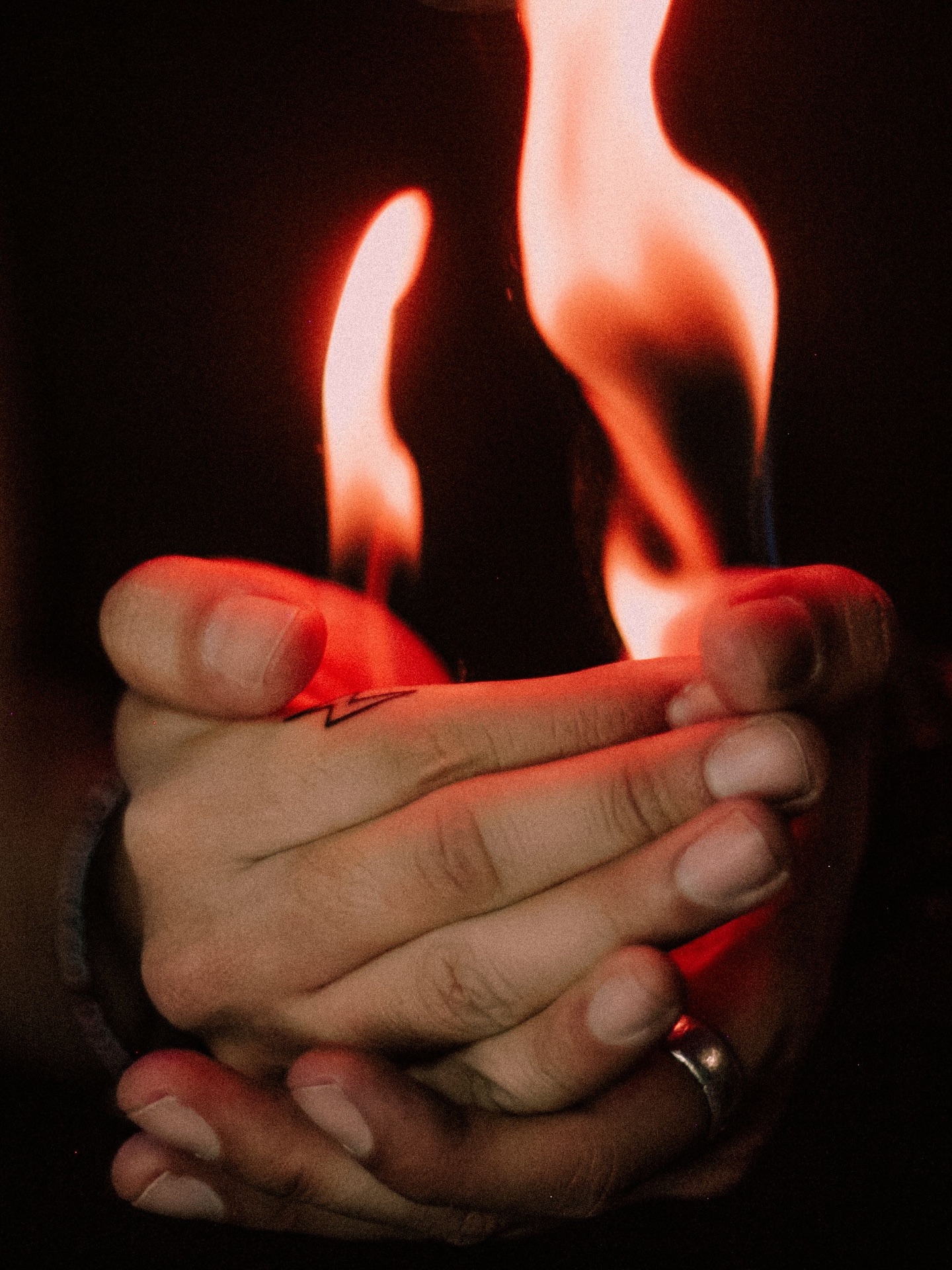A pair of hands cupping a single flame in the dark
