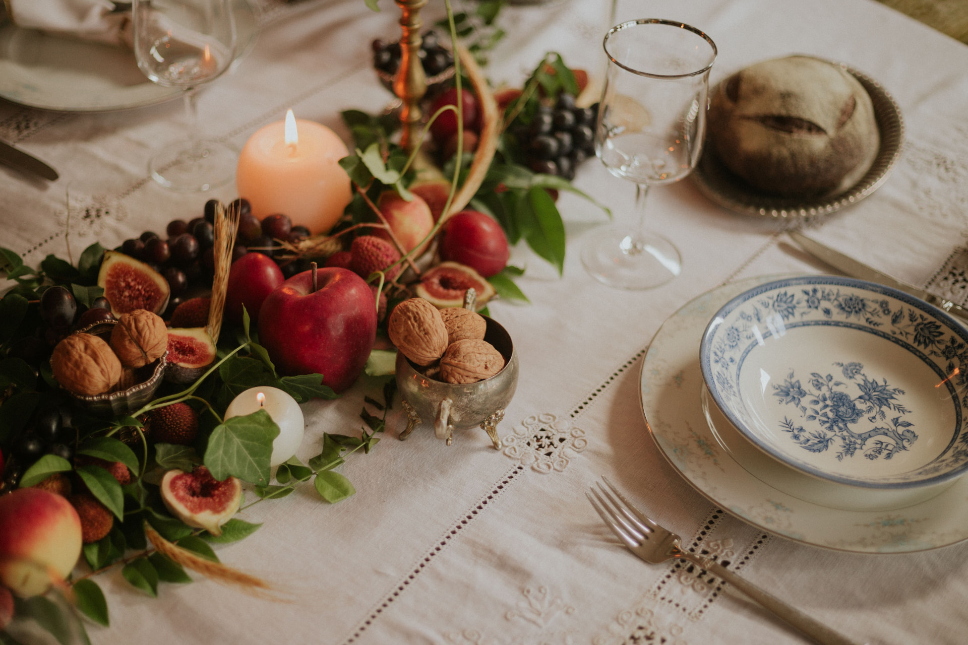 A candlelit autumn table set with blue and white china, fruit, nuts, and a fresh loaf of bread