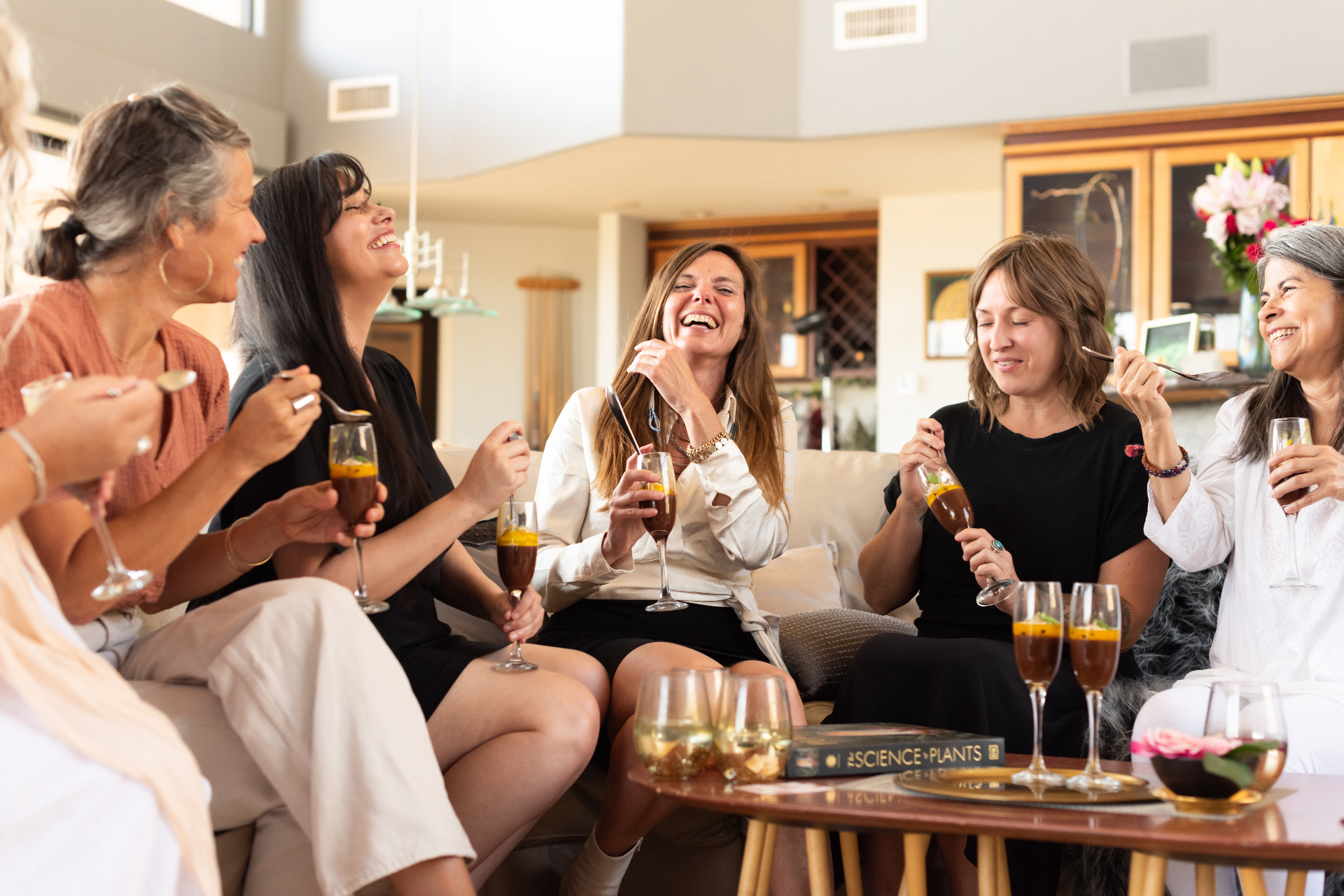 A circle of women laughing together on the couch, passion fruit chocolate mousse in coupes