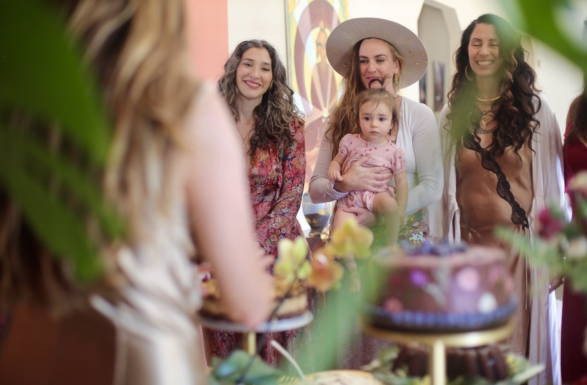 A circle of women gathered around cakes and flowers