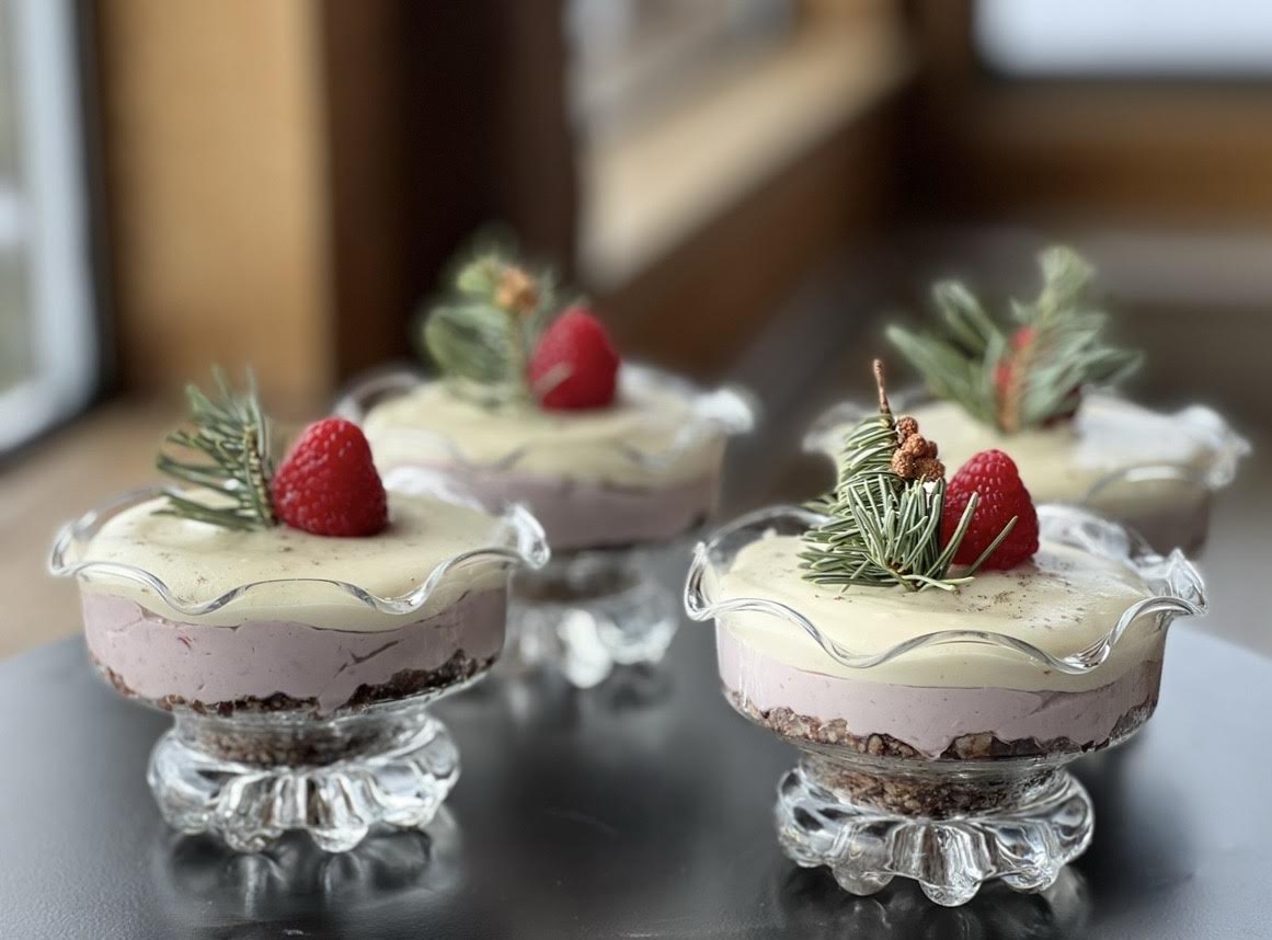 Raspberry cheesecakes in fluted glass dishes with fir sprigs