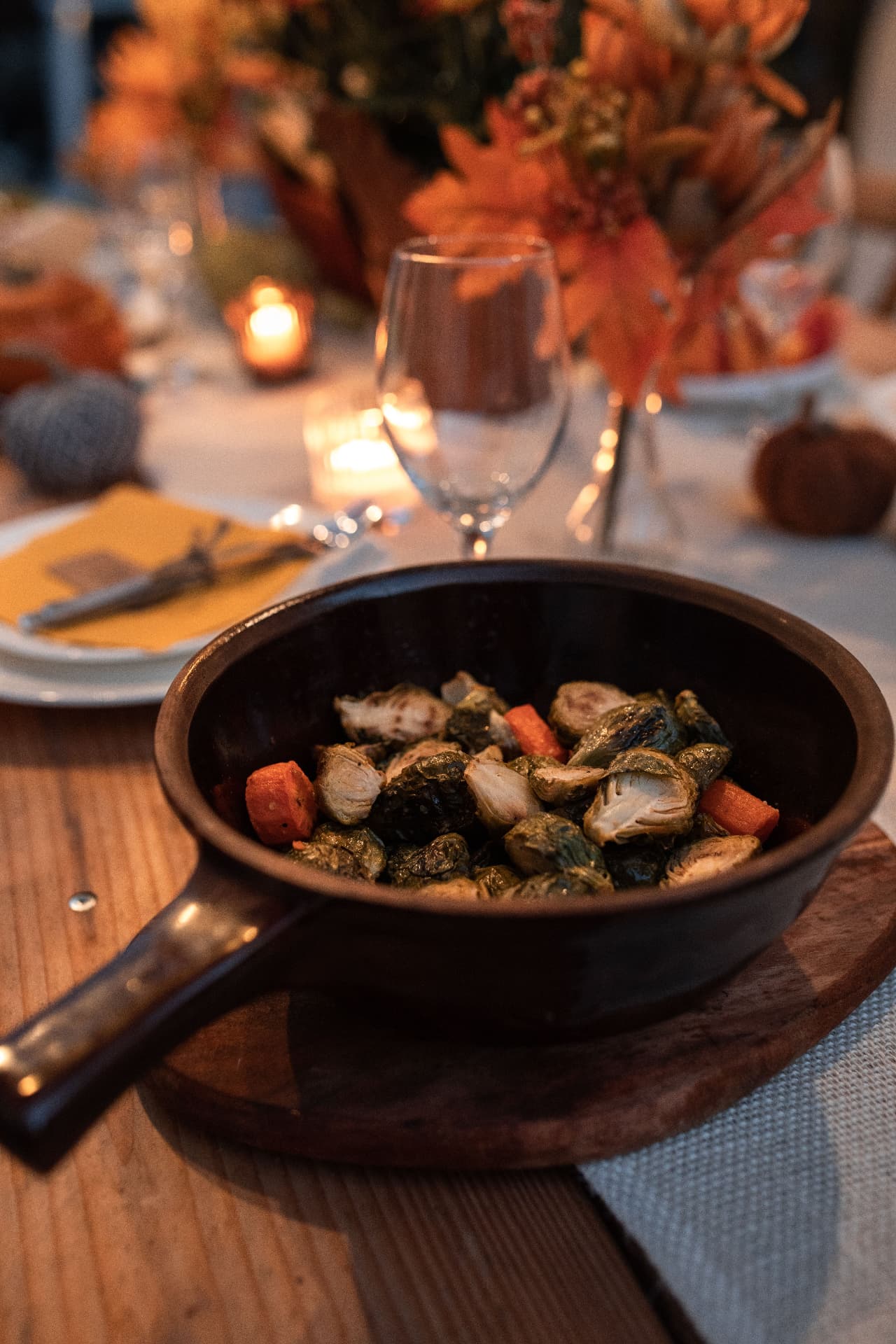 A cast-iron skillet of roasted brussels sprouts and carrots on a candlelit autumn table