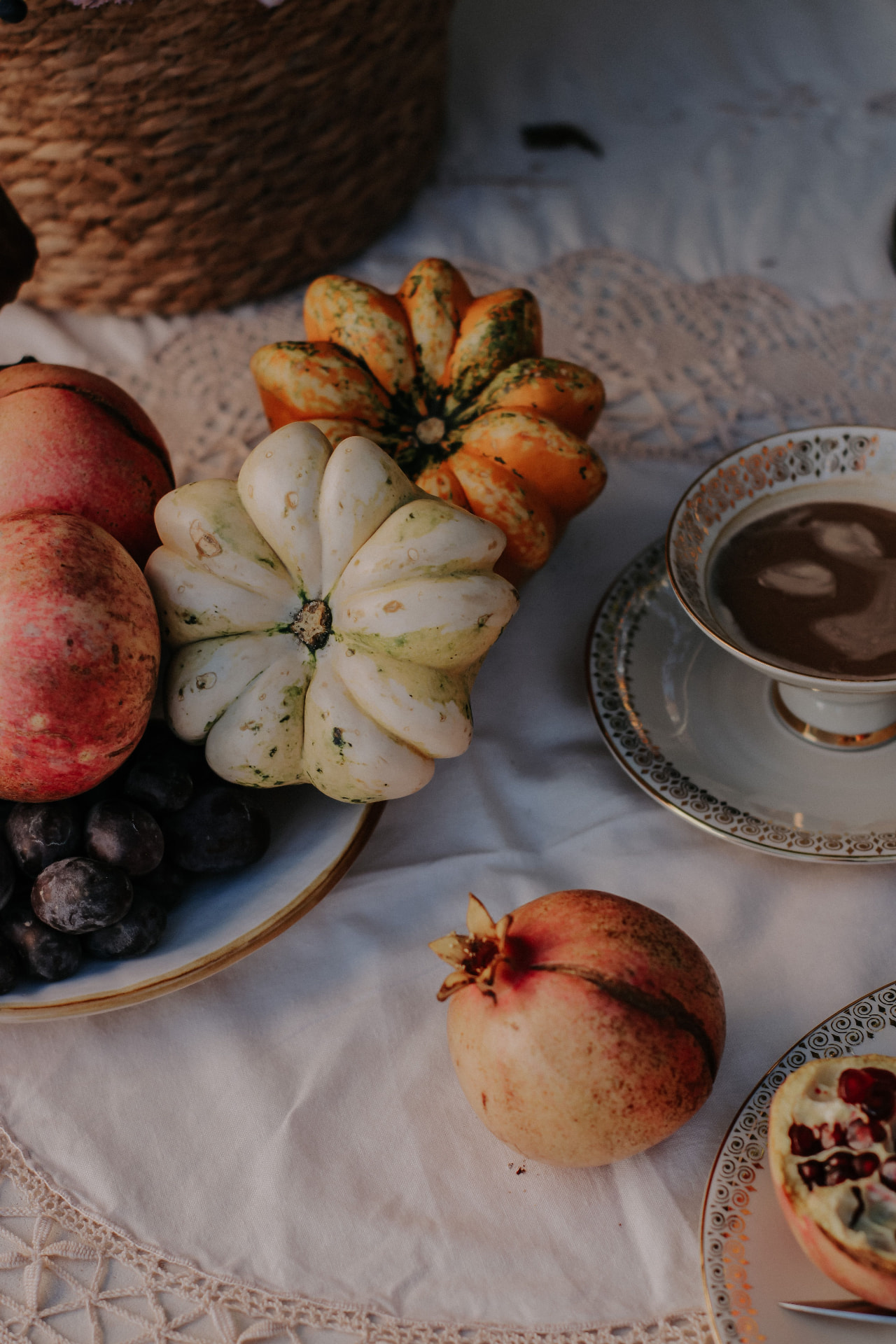 Gourds, pomegranates, and a porcelain cup of chocolate on white linen