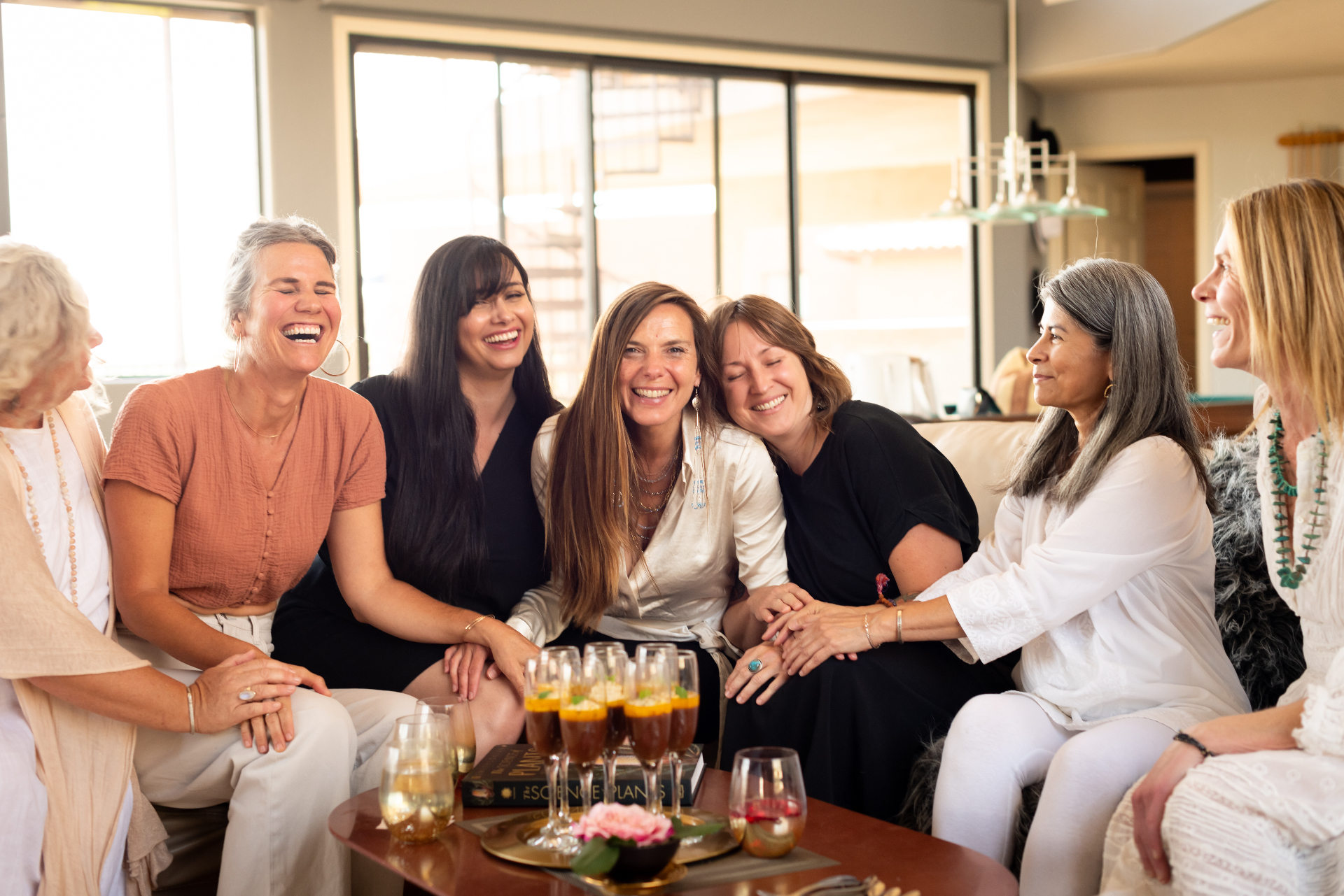 Caitlin laughing on the couch surrounded by a circle of women, dessert glasses on the table before them