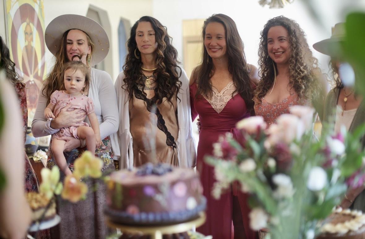 Four women standing together behind a chocolate floral cake, the salon assembled