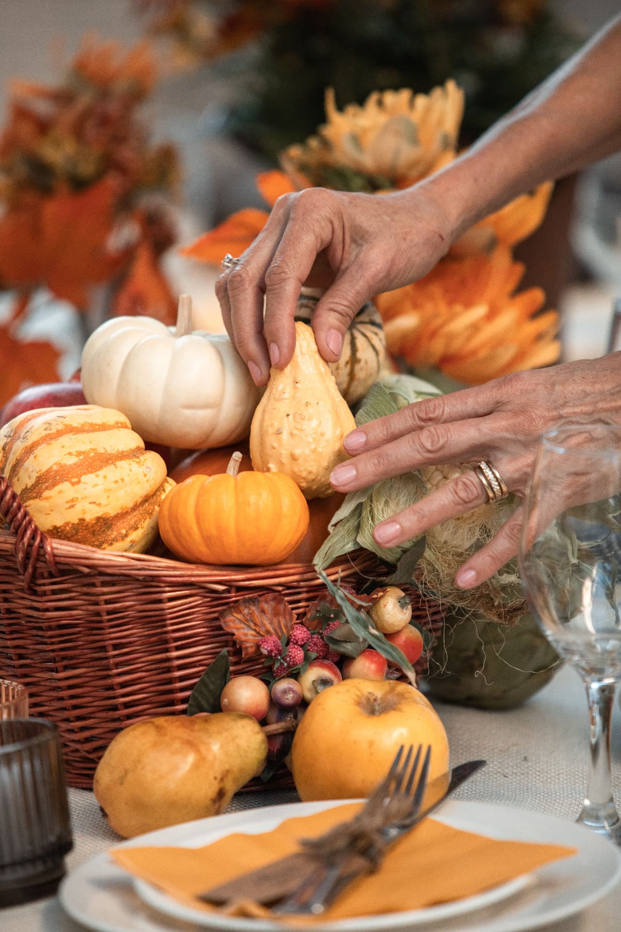 Hands arranging gourds and small pumpkins in a wicker basket centerpiece