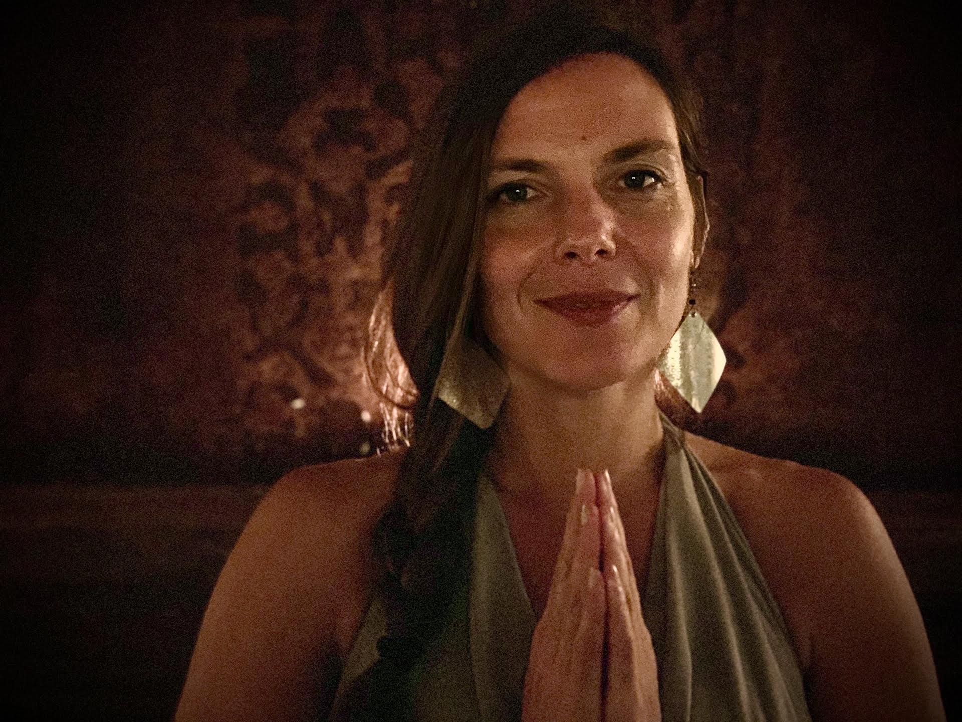 Caitlin Naramore with hands in prayer, warm candlelight behind her